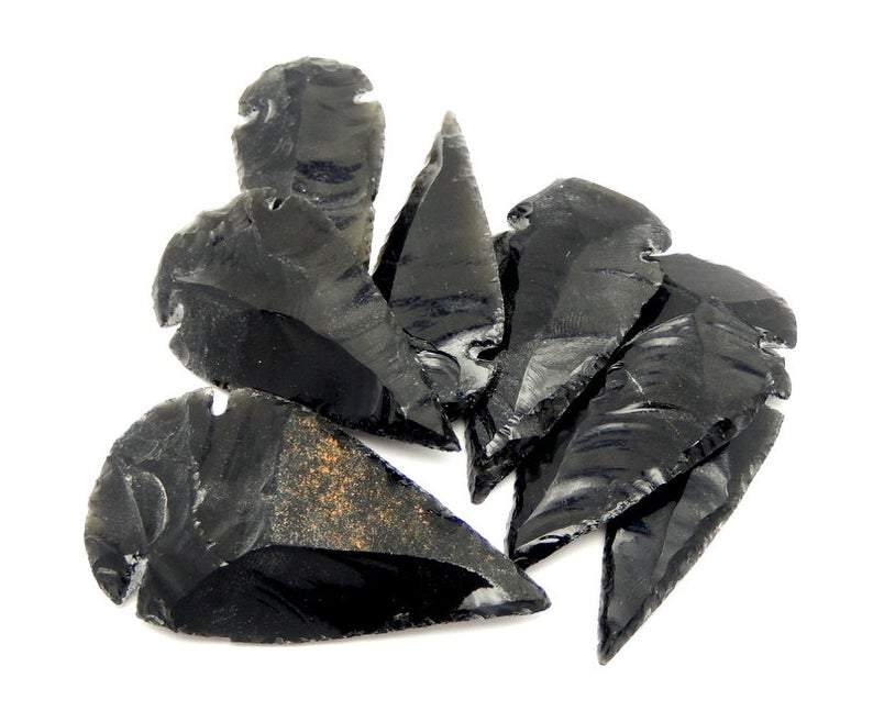 An assortment of black obsidian arrowheads to show that they vary slightly in shape and size on a white background.