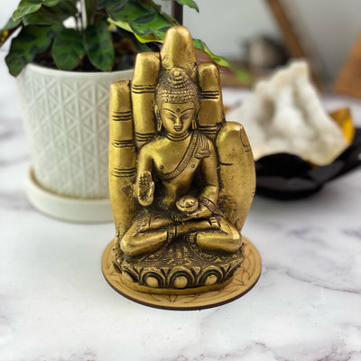 A brass hand with a buddha sitting inside of it.