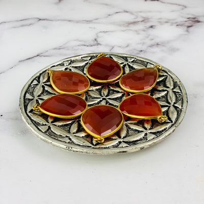 side view close up of 6 carnelian teardrops on a brass plate with a white marble background