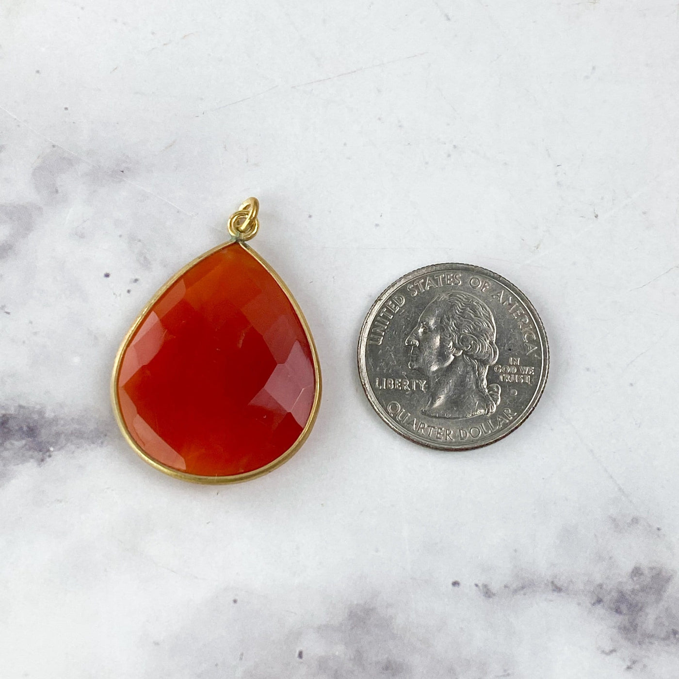 one carnelian teardrop next to a quarter on a marble background