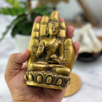 A brass hand with a buddha sitting inside of it held in a hand.