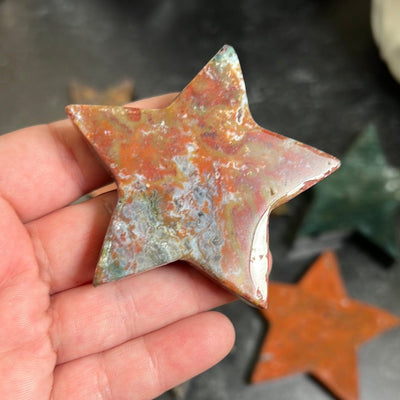 Red jasper with white and yellow banding star in a woman's hand.