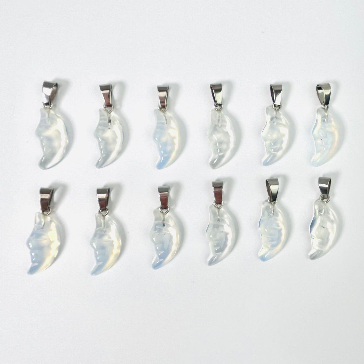 Twelve Opalite Crescent Moon Gemstones Pendants lined up in two rows on a white surface.