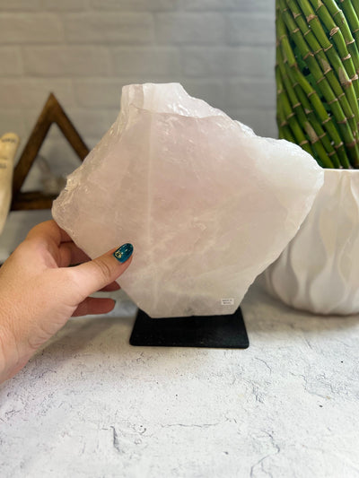 Rose Quartz large slab on a black metal base with a woman's hand next to it.
