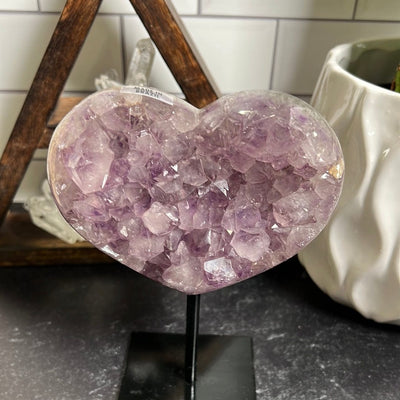 Close up of amethyst heart on a black metal stand on a black background.