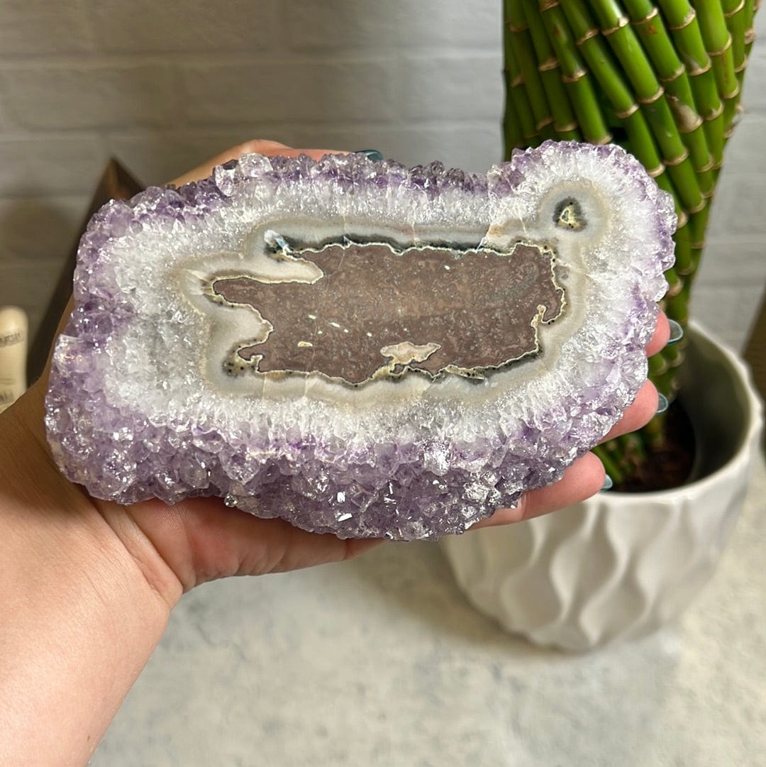 Amethyst stalactite formation.  The stalactite shows on the top and the bottom side is purple amethyst clusters.  Held in a woman's hand.