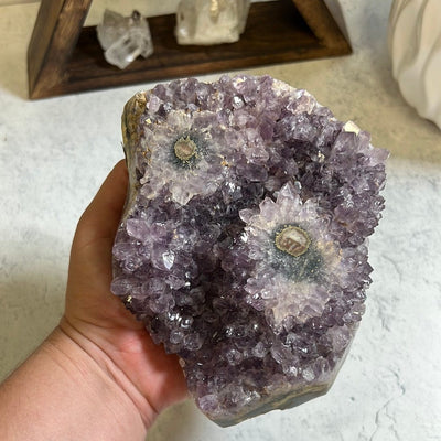 Amethyst stalactite cluster.  It has two stalactite eyes on the top. In a woman's hand.