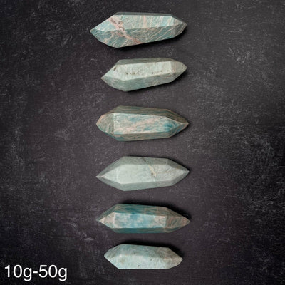 Six different variations of the Amazonite Polished Double Terminated Points, in the weight range of 10g-50g, lined up on a black surface.
