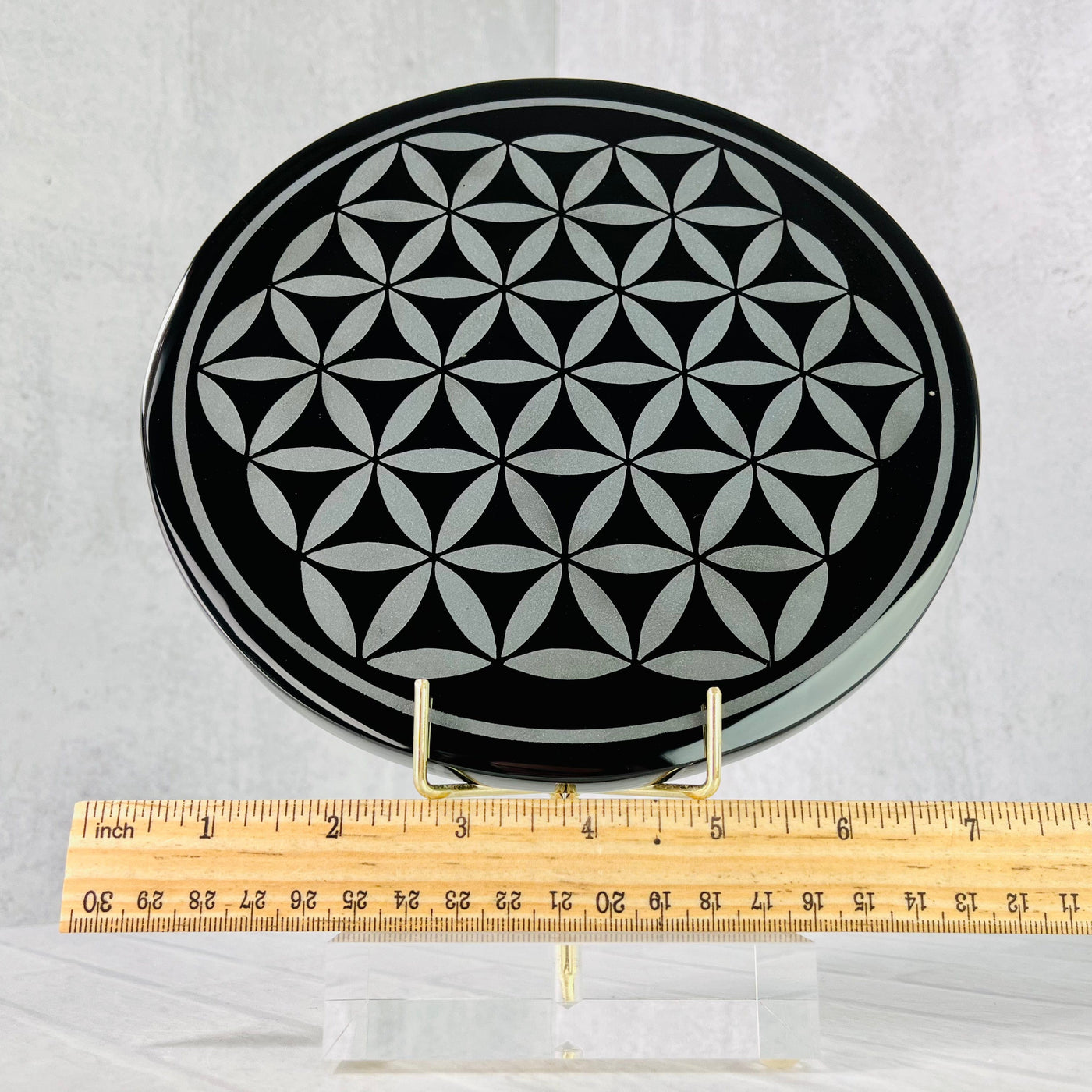 Frontal view of Black Obsidian Flower of Life Plate on a stand, with a ruler placed below it for size reference.