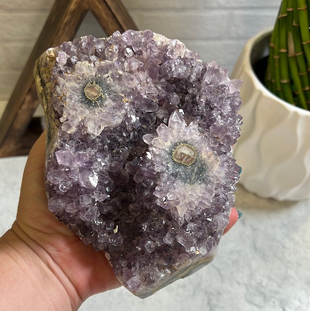 Amethyst stalactite cluster.  It has two stalactite eyes on the top. In a woman's hand.