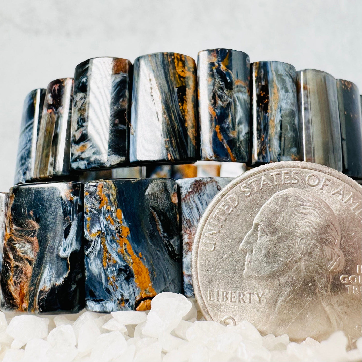Stacked Blue Pietersite Rectangle Bead Bracelets next to a quarter for size reference.