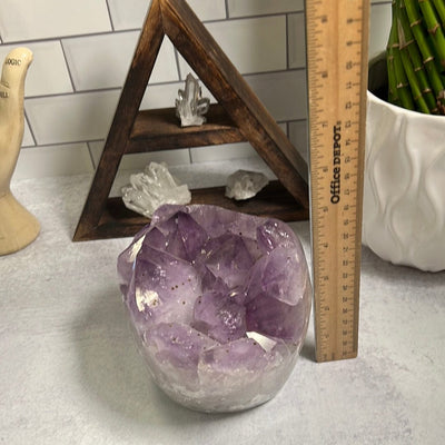 Amethyst cluster with polished sides.  The sides are more white and the top clusters are purple with some black speckles.  Next to a ruler showing it is around 5 inches tall.