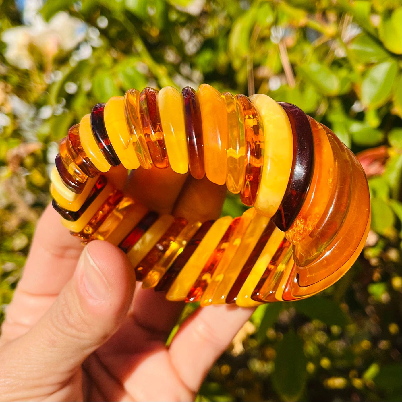 Side angle view of Baltic Amber Bracelet, held up by woman's hand.