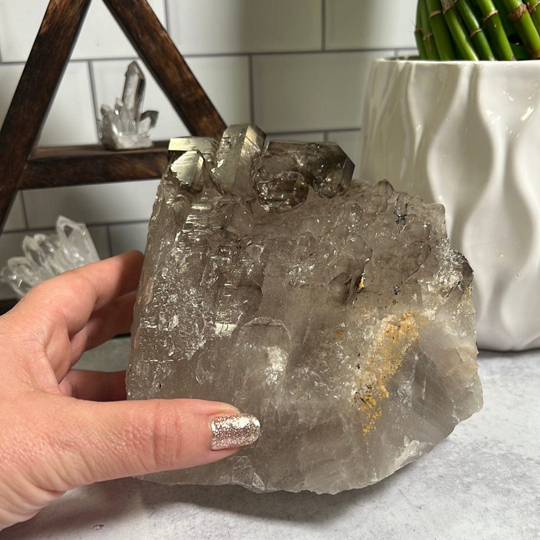 Large natural smokey quartz cluster with a woman's hand touching it.