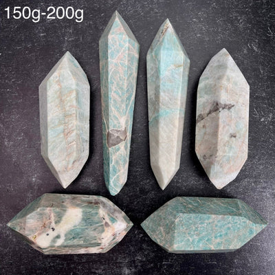 Six different variations of the Amazonite Polished Double Terminated Points, in the weight range of 150g-200g, laid out on a black surface.