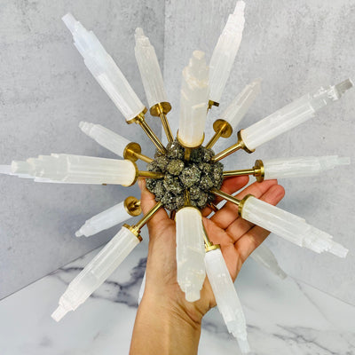 Selenite Point Spike Globe with Pyrite Cluster Center held up in a woman's hand.