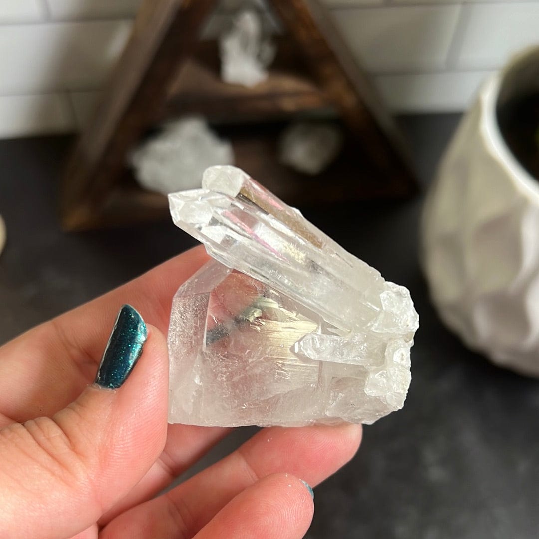 Crystal cluster with multiple points in it held in a woman's hand with a black background.