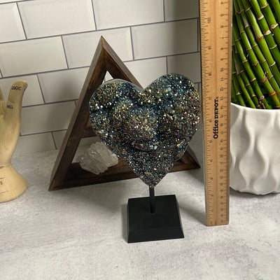 Amethyst heart coated with rainbow titanium on a black wood stand.  With a ruler showing it is around 8 inches tall.