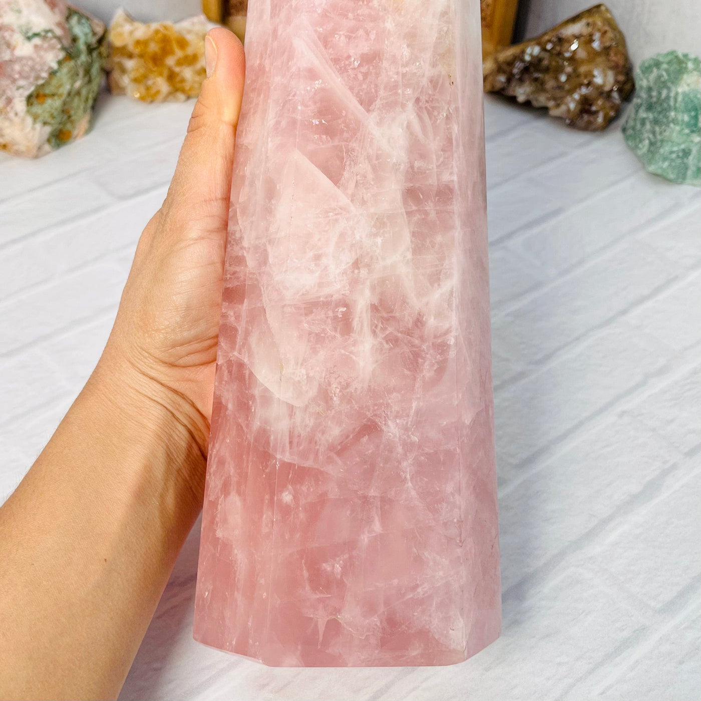 Up close view of the lower half of the Rose Quartz Polished Tower, held up in woman's hand.