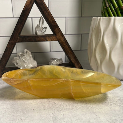 Yellow flourite bowl in front of a wood triangle small shelf with crystals on it.