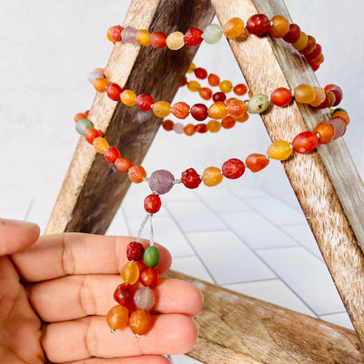 Gobi Desert Agate Mala Bead Necklace displayed on a wooden triangle, wrapped around and hanging down center. Up close of a woman's hand showing the center piece of the necklace.