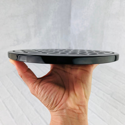 Black Obsidian Flower of Life Plate side view, held up by woman's hand.