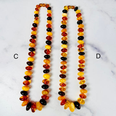 Amber necklaces C and D displayed on a flat surface side by side.