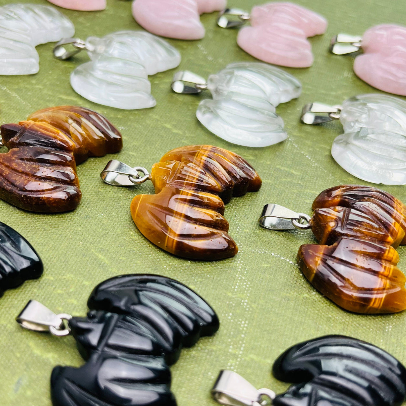 Up close side angle of sixteen Bat Gemstone Pendants spread out on a green surface.
