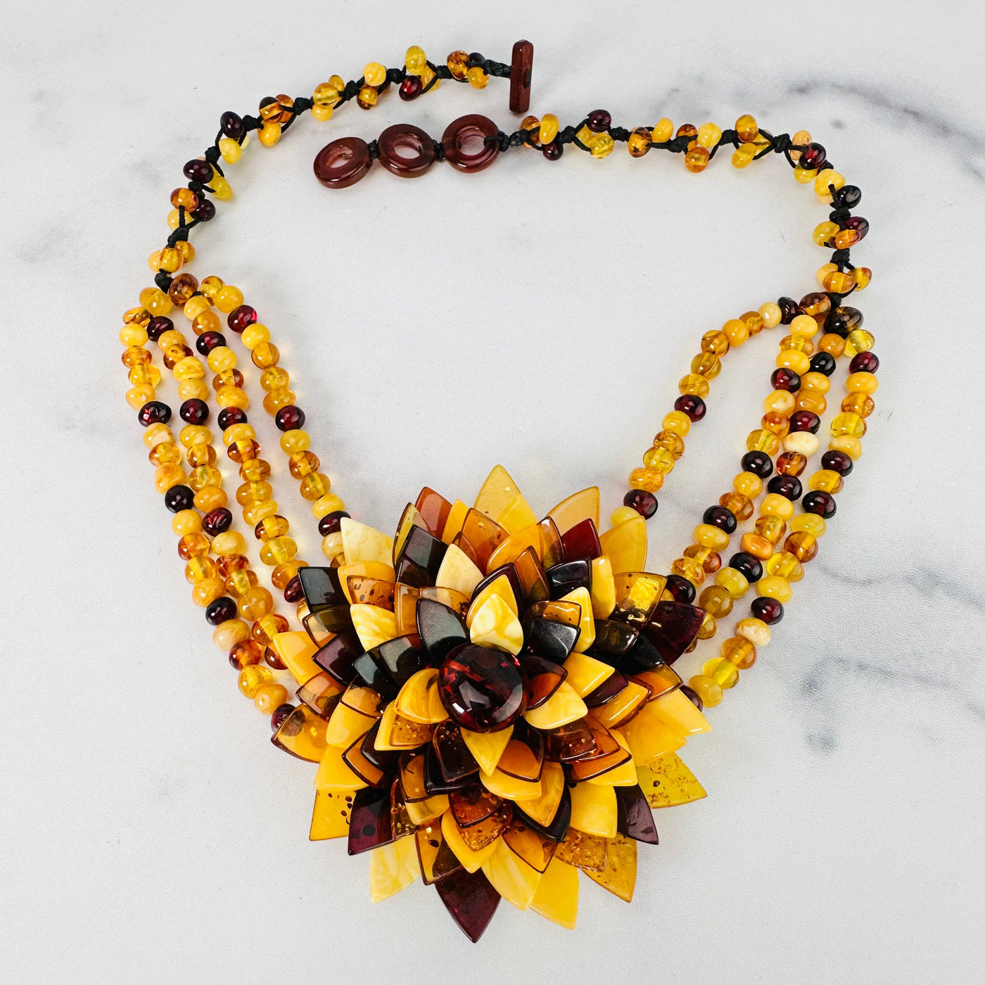 Frontal view of Multi-colored Baltic Amber Beaded Flower Necklace shown on a marble surface with closure undone.