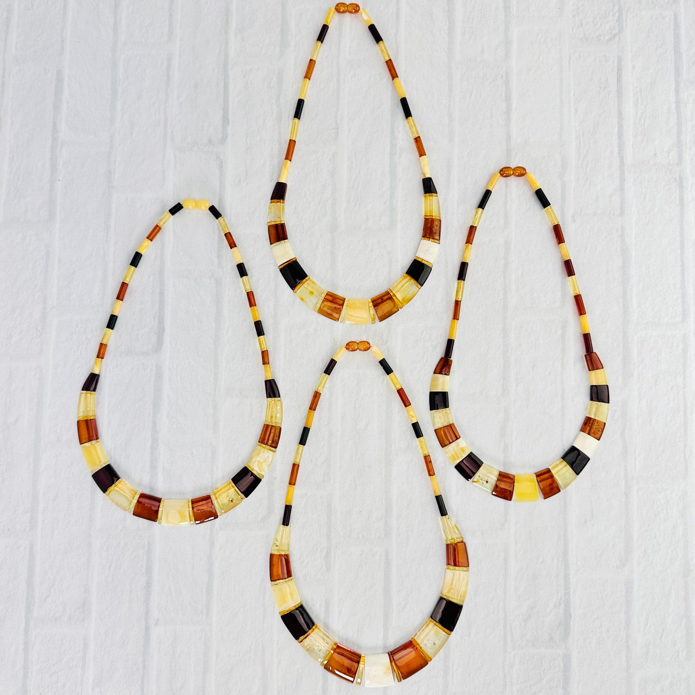 Aerial view of necklaces, F, G, H and I, on a white surface.