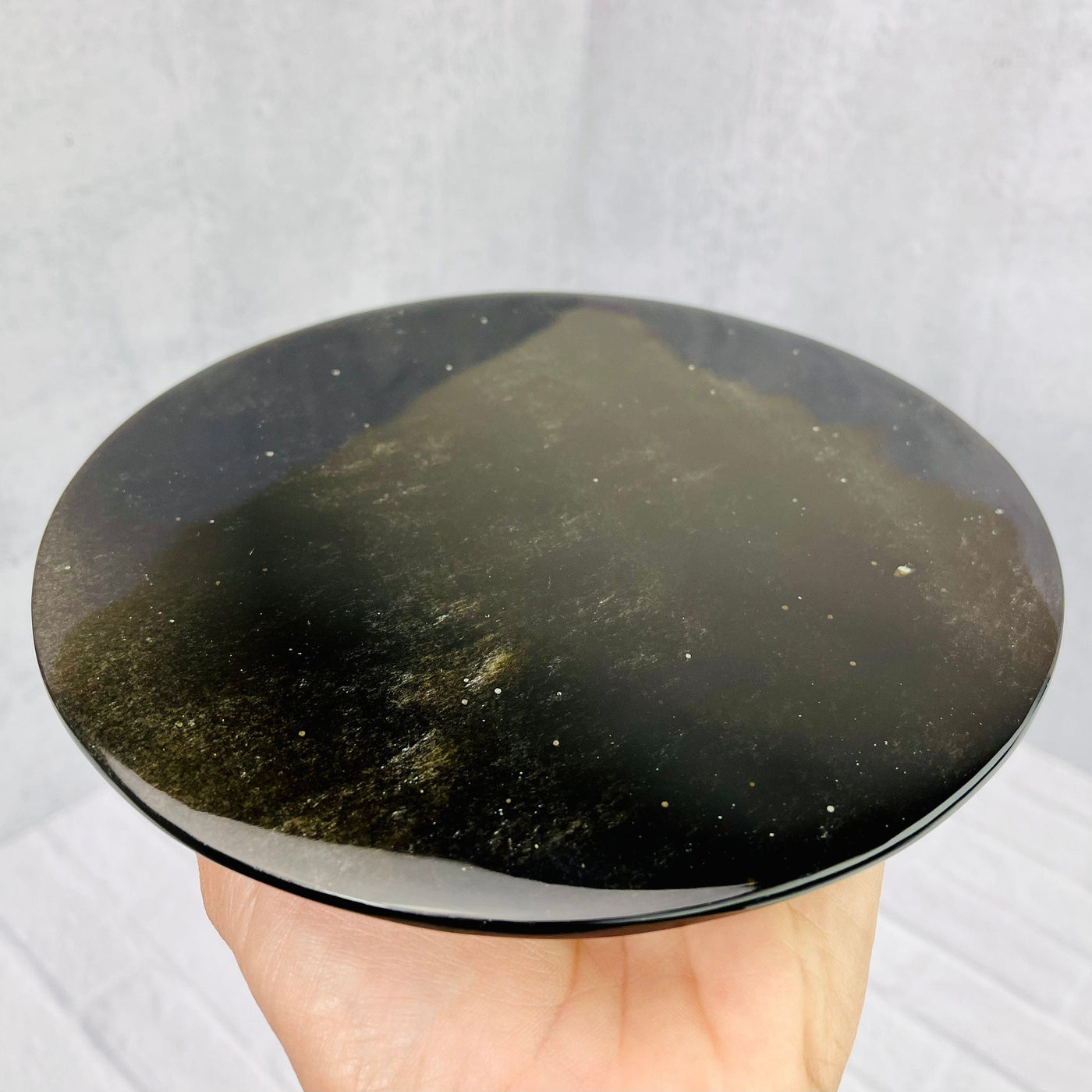 Bottom view of  Gold Sheen Obsidian Flower of Life Plate, held up in woman's hand.