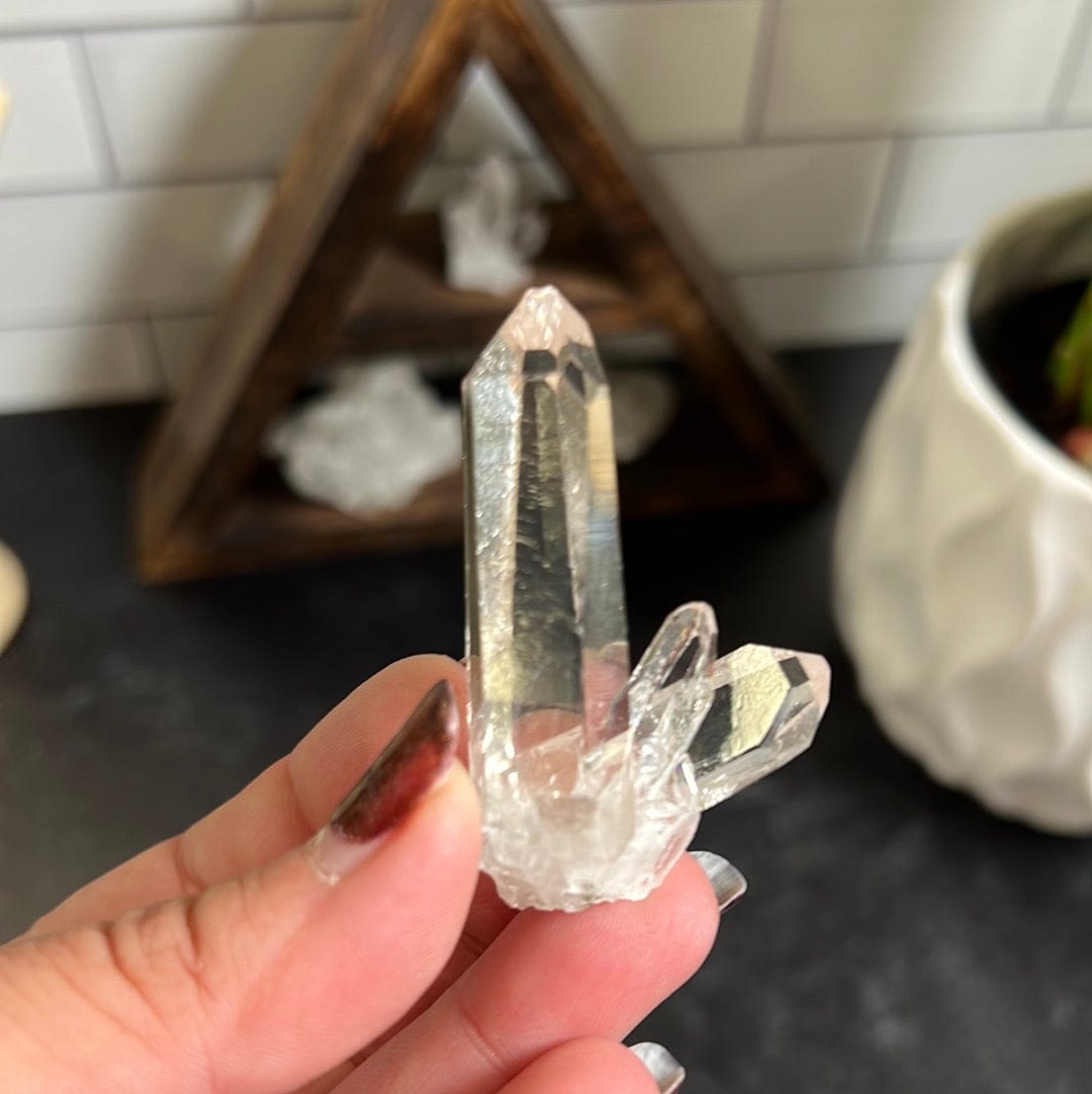 Crystal cluster in a woman's hand.  It has one larger point and 3 smaller points coming out the right side.