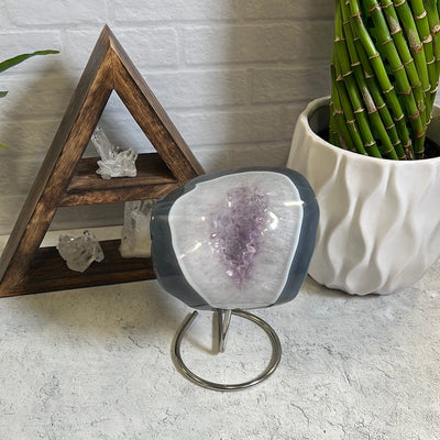 Agate polished stone with amethyst in the center on a silver metal base pictured on a gray background.