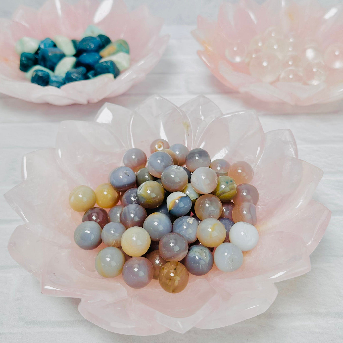 3 Rose Quartz Lotus Bowls displayed with small stones in them.