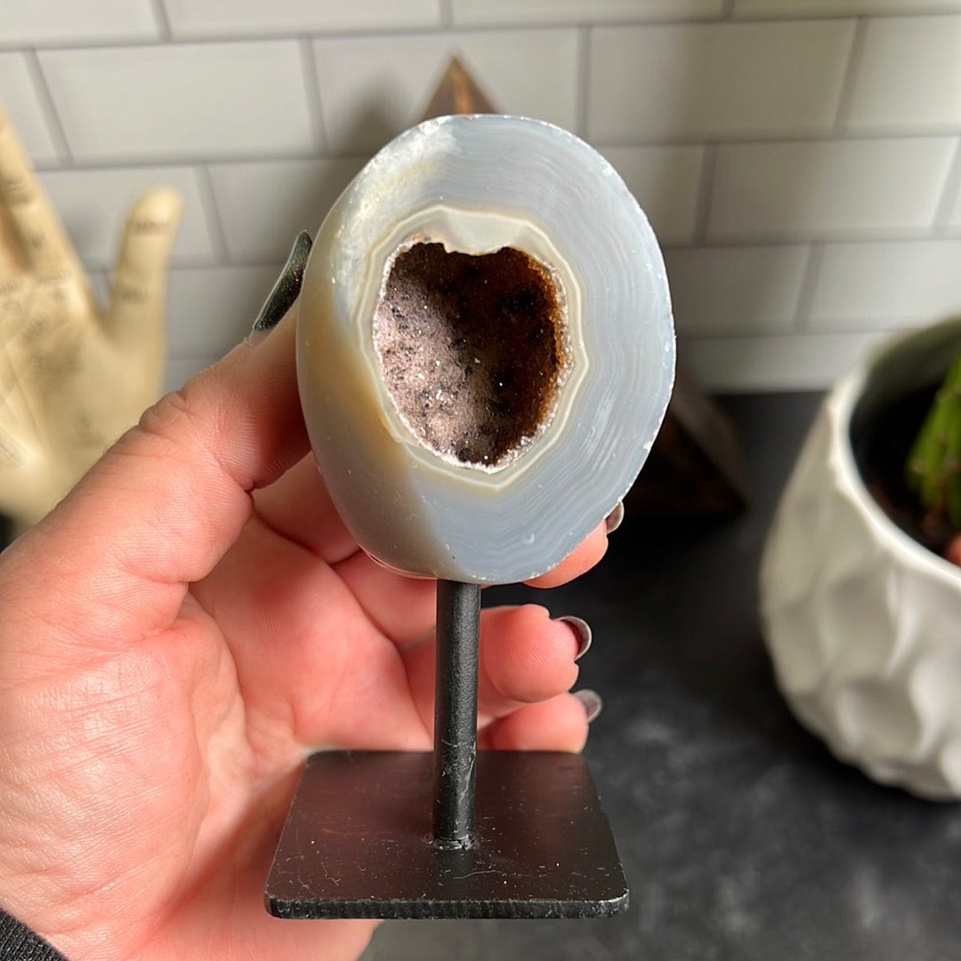 Agate geode on a metal stand.  It has a gray outer shell with a light purplish brown druzy center.