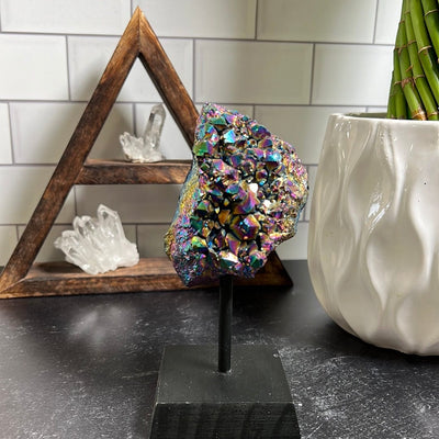 Amethyst cluster coated in titanium to make it rainbow colors on a black wood stand.