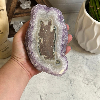 Amethyst stalactite formation.  The stalactite shows on the top and the bottom side is purple amethyst clusters.  Held in a woman's hand in this photo.