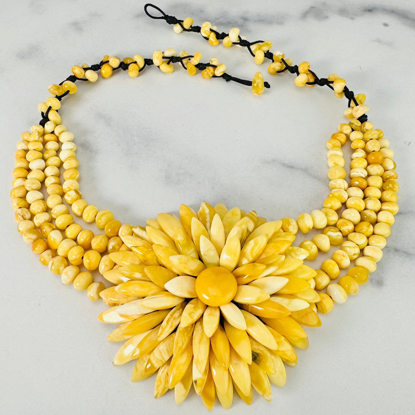 Frontal view of Yellow Baltic Amber Beaded Flower Necklace shown on a marble surface with closure undone.