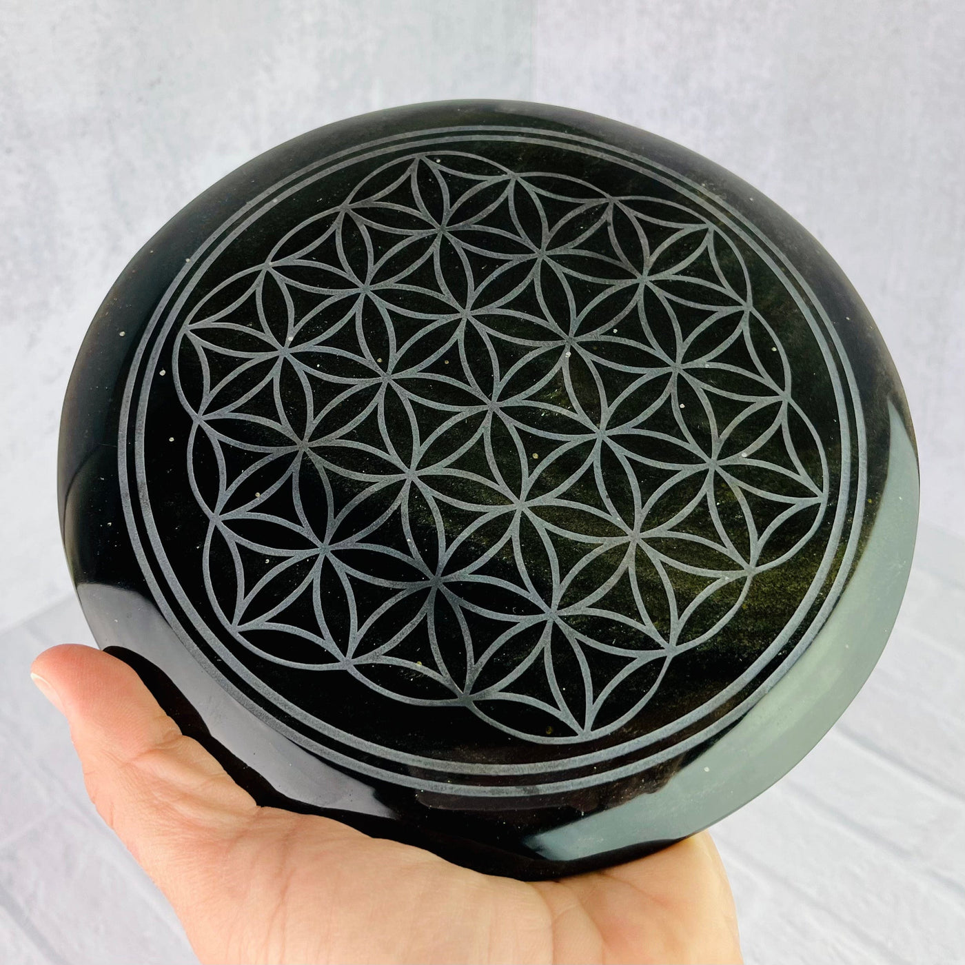 Aerial view of  Gold Sheen Obsidian Flower of Life Plate held in woman's hand.