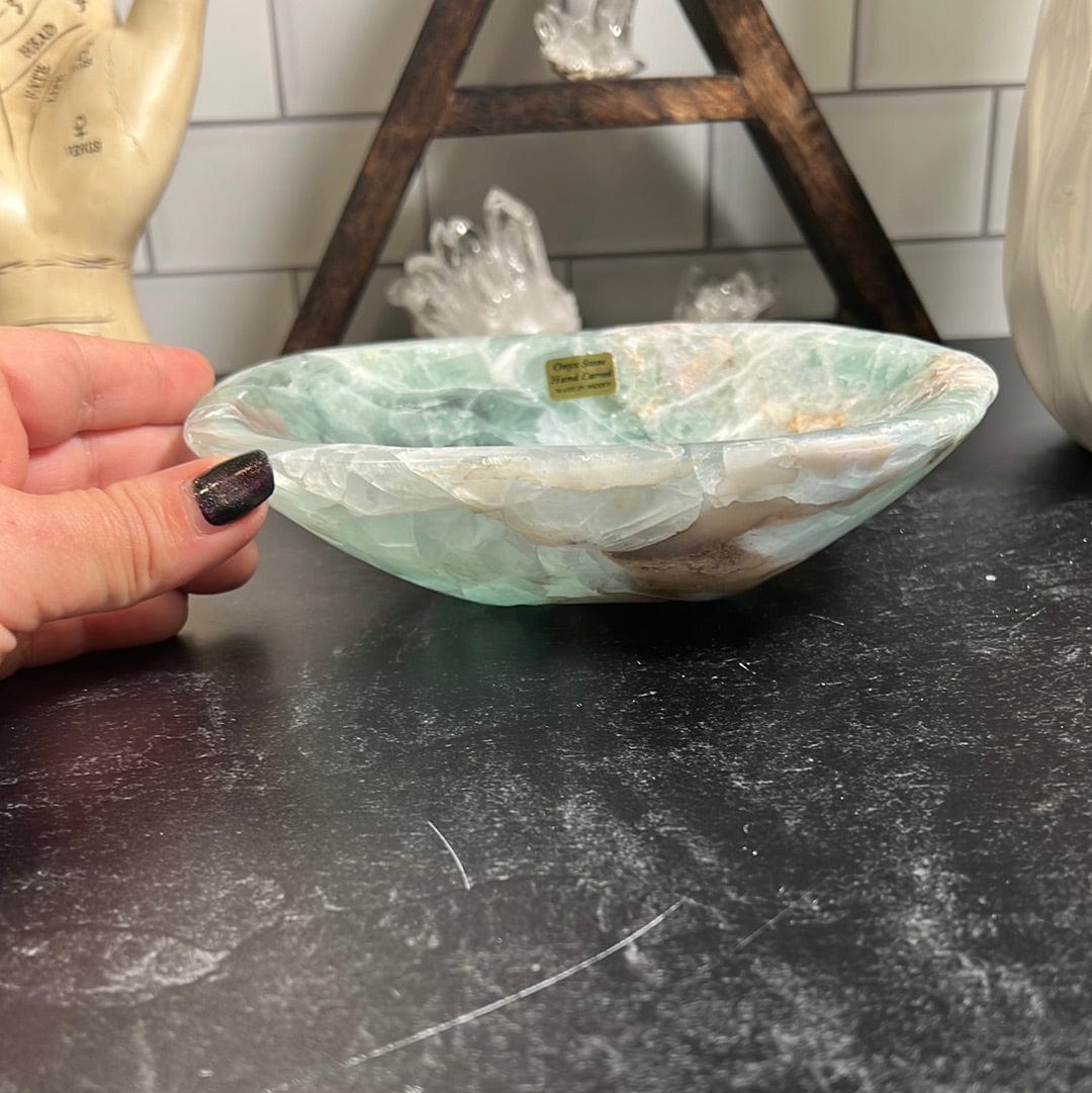 Green fluorite bowl on a black background with a woman's hand touching the side of it.
