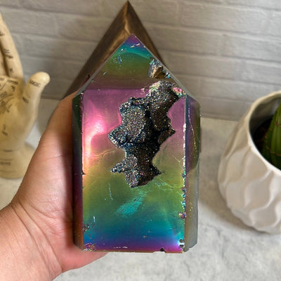 Rainbow titanium agate slice with a druzy center and some other openings on the stone.  It has some natural dent marks along the front held in a woman's hand.