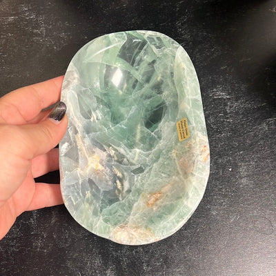 Green fluorite bowl on a black background with a woman's hand touching the side of it.