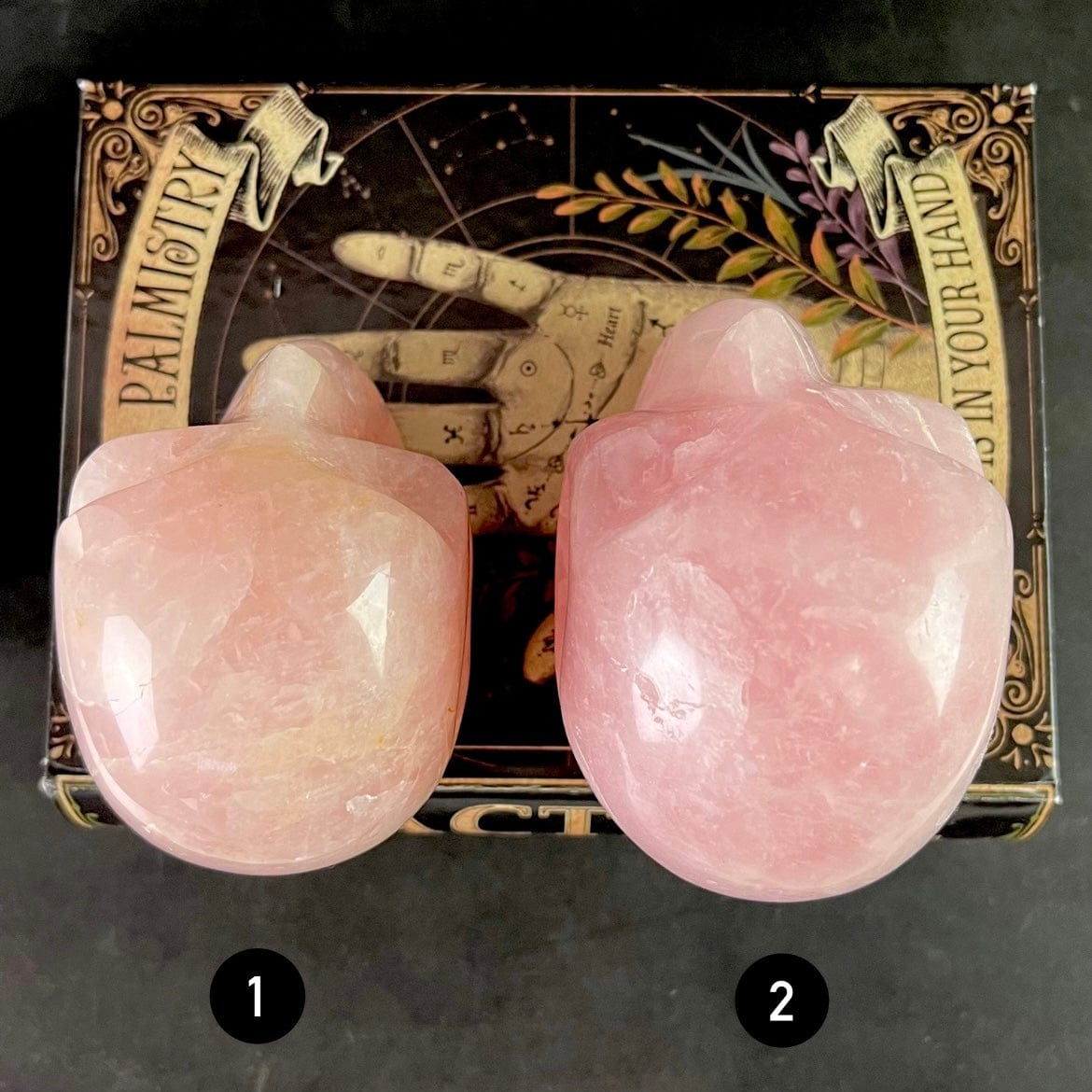 Aerial view of Rose Quartz Polished Skulls, placed on top of book with numbers 1 and 2 listed below the appropriate skull.
