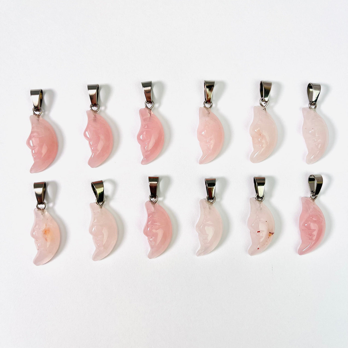 Twelve Rose Quartz Crescent Moon Gemstones Pendants lined up in two rows on a white surface.
