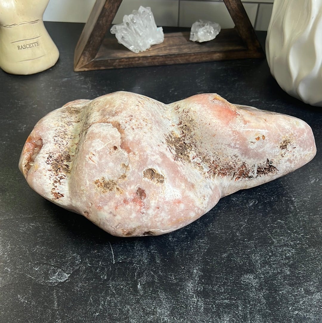 Large pink amethyst geode freeform in shape. It is long with three humps rising on the top It is polished and contains shades of pink and druzy pockets mostly in the center.