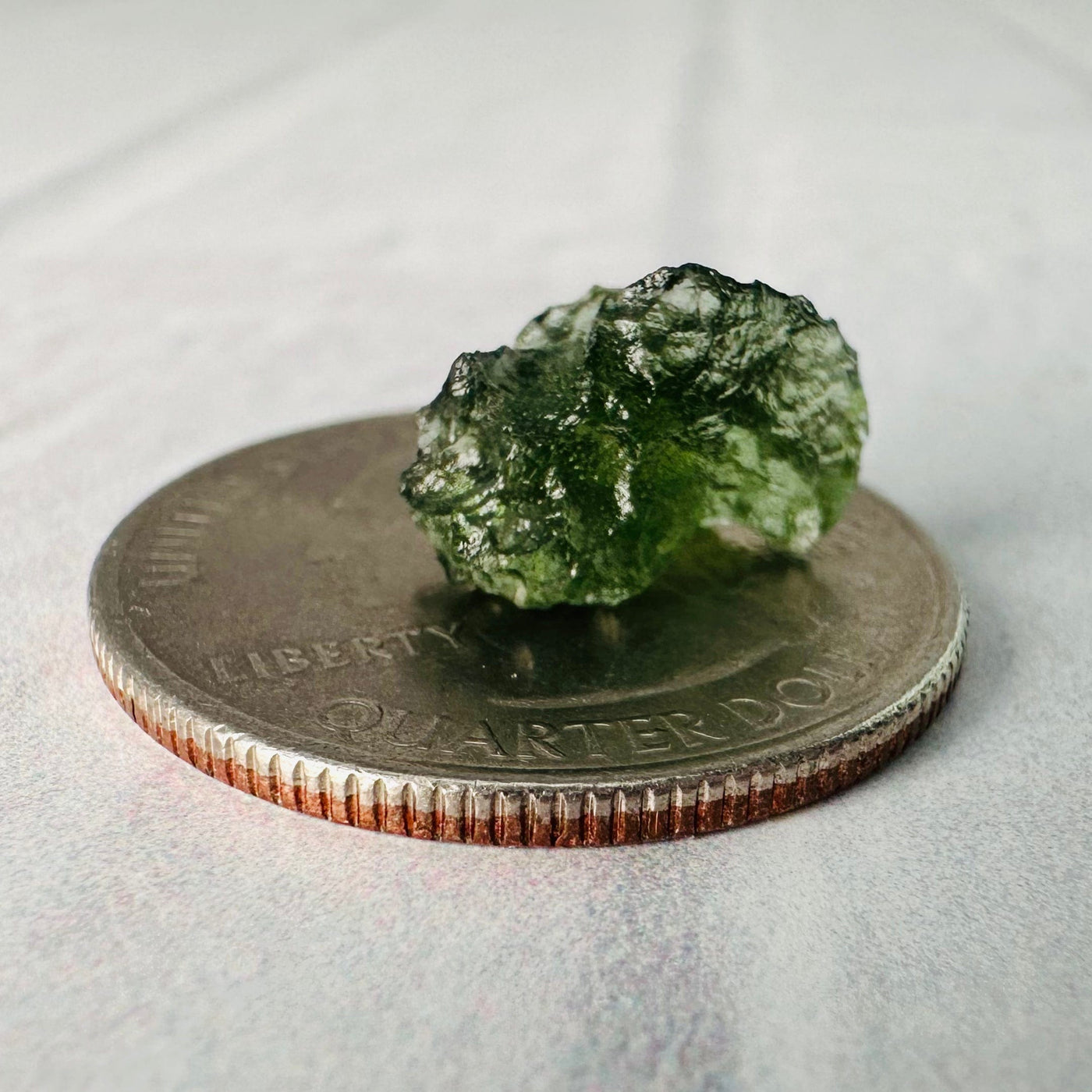 0.6 gram (option A) Moldavite piece on top of a quarter for size reference.