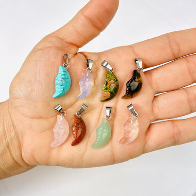 Eight Crescent Moon Gemstone Pendants set up in 2 lines; one of each stone displayed in palm of a woman's hand.