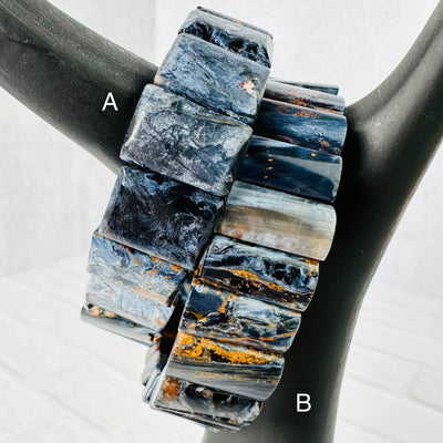 Up close view of both Blue Pietersite Rectangle Bead Bracelets on a black ceramic hand display, also with respective letter next to them.
