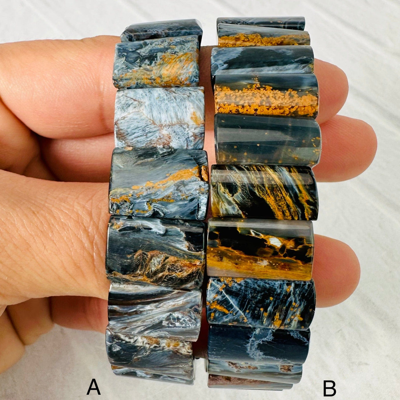 Up close view of Blue Pietersite Rectangle Bead Bracelets side by side over woman's fingers. Respective letters on lower part of picture next to the bracelet they represent.