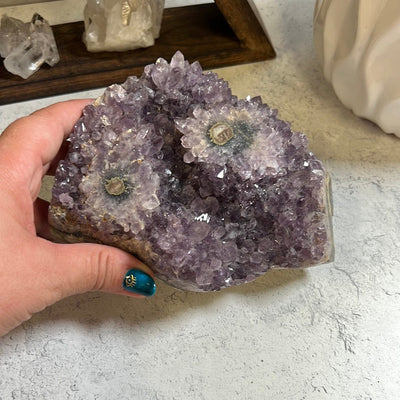 Amethyst stalactite cluster.  It has two stalactite eyes on the top.  A woman's hand is touching the piece.